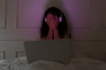 Žena sedí u notebooku a vystrašeně si zakrývá oči.