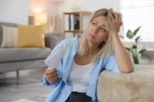 Žena sedící u gauče podpírající si hlavu.