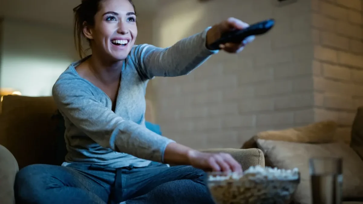 veselá žena z gauče přepíná televizi a jí popcorn