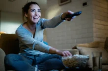 veselá žena z gauče přepíná televizi a jí popcorn