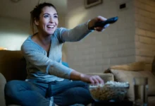 veselá žena z gauče přepíná televizi a jí popcorn