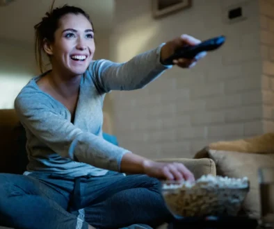 veselá žena z gauče přepíná televizi a jí popcorn