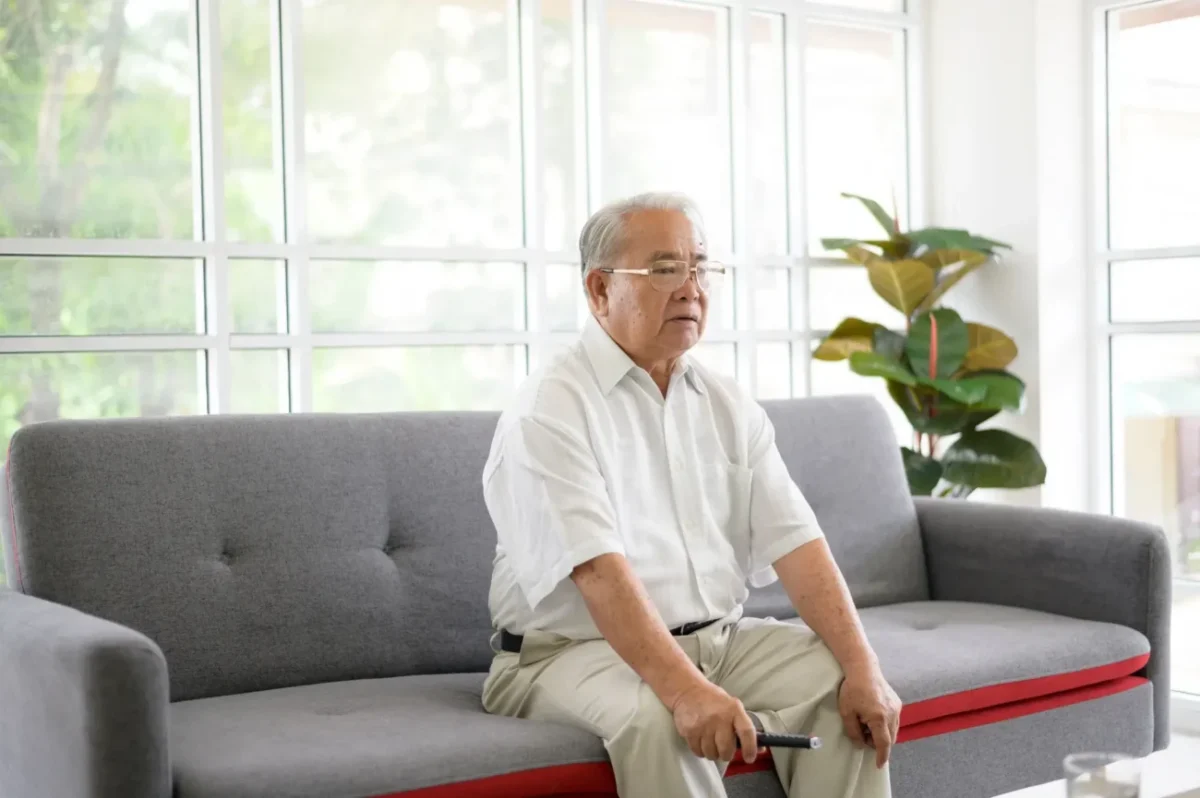 starý muž sedí na gauči s ovladačem v ruce a tváří se zaraženě