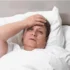 Babička leží v posteli a chytá se za čelo.