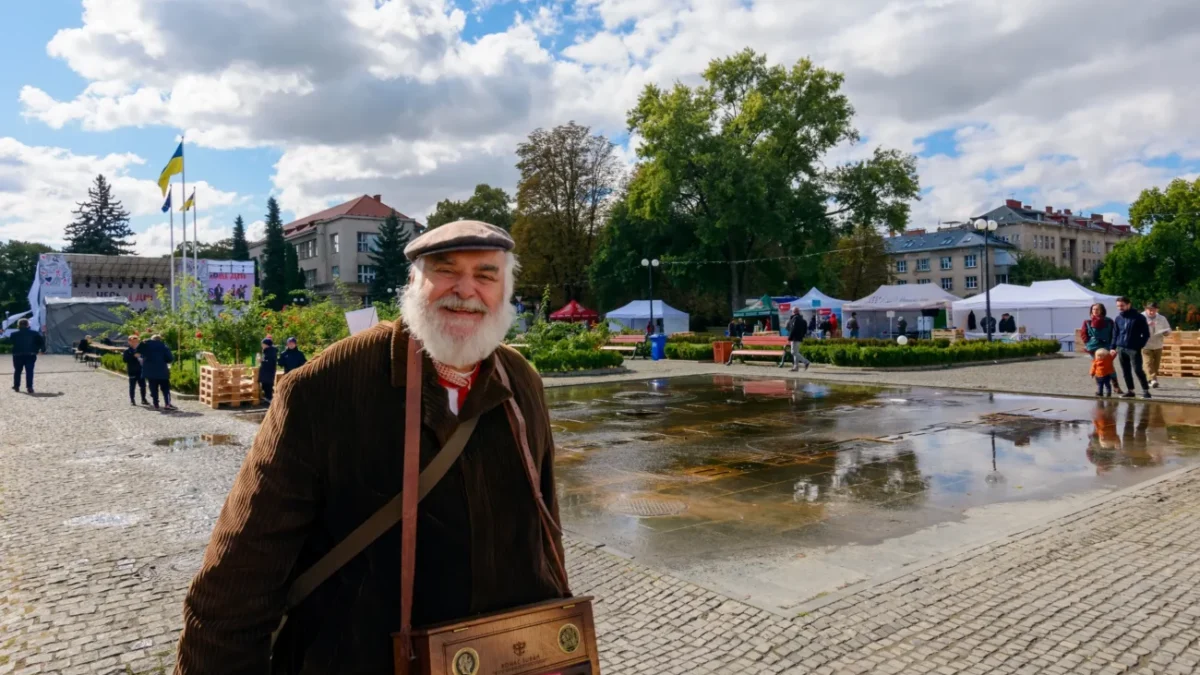 Starý muž stojí na náměstí a usmívá se.