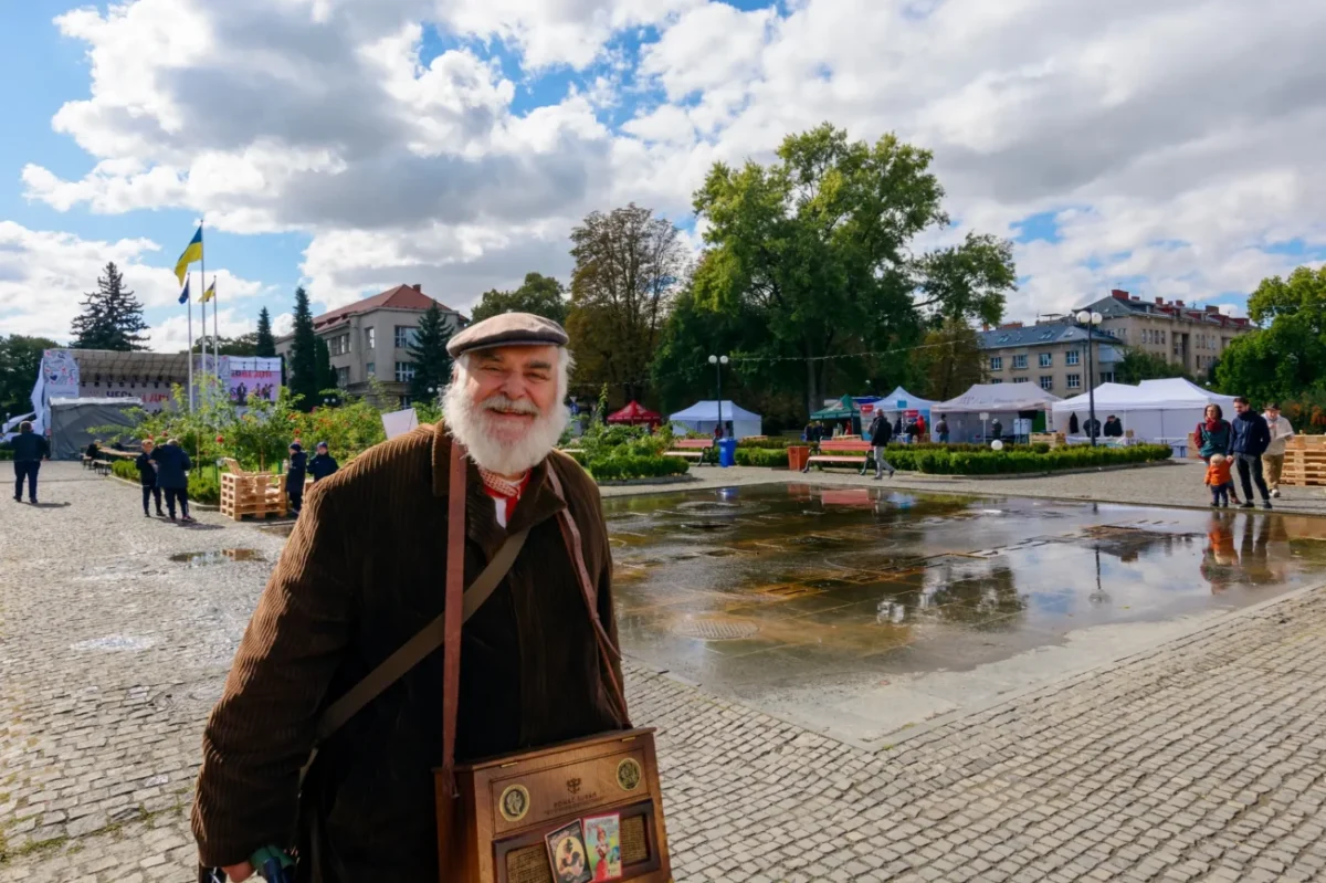 Starý muž stojí na náměstí a usmívá se.