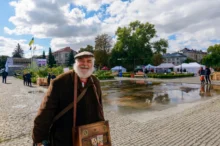 Starý muž stojí na náměstí a usmívá se.