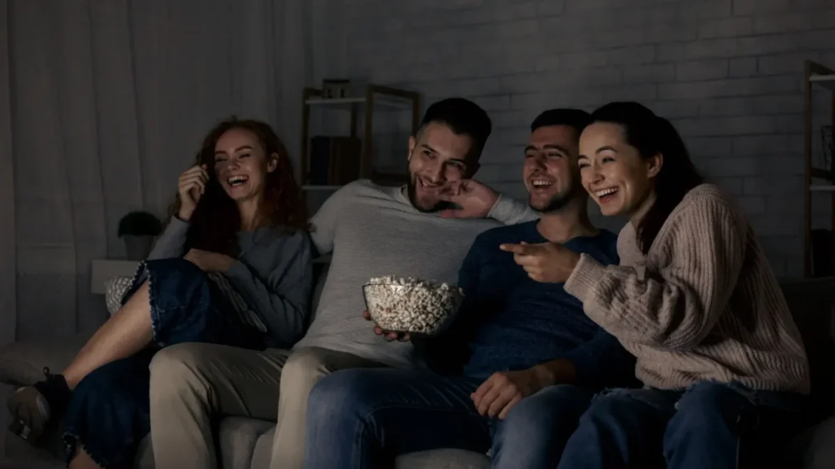 skupina mladých lidí pobaveně sleduje televizi