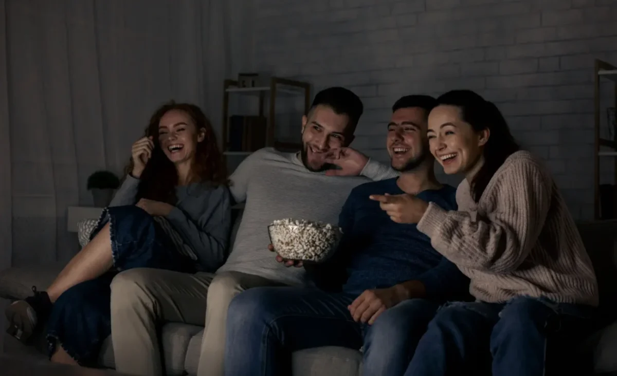 skupina mladých lidí pobaveně sleduje televizi