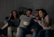 skupina mladých lidí pobaveně sleduje televizi