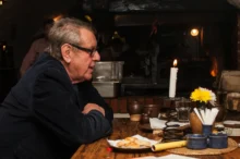 Miloš Forman sedí u stolu.