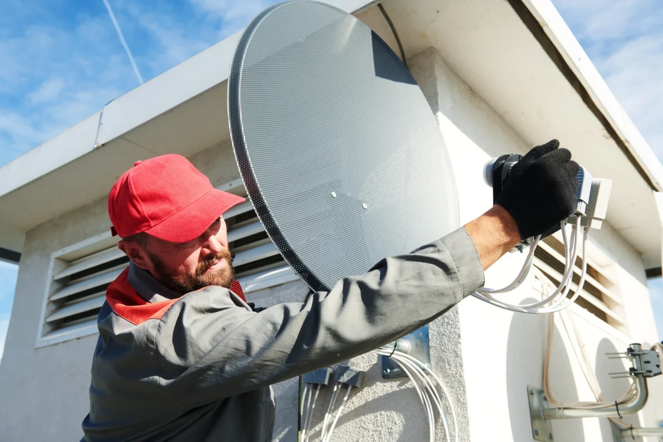 Muž na střechu instaluje satelit. 