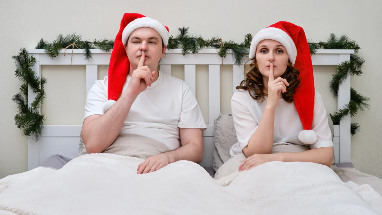 shutterstock_2206365045-2 | TVGURU.cz Muž a žena na sobě mají santovskou čepici a leží vedle sebe v posteli.
