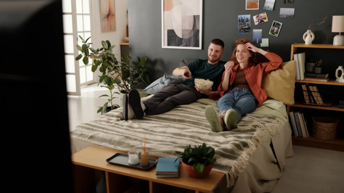 Žena a muž leží na posteli a dívají se na televizi.