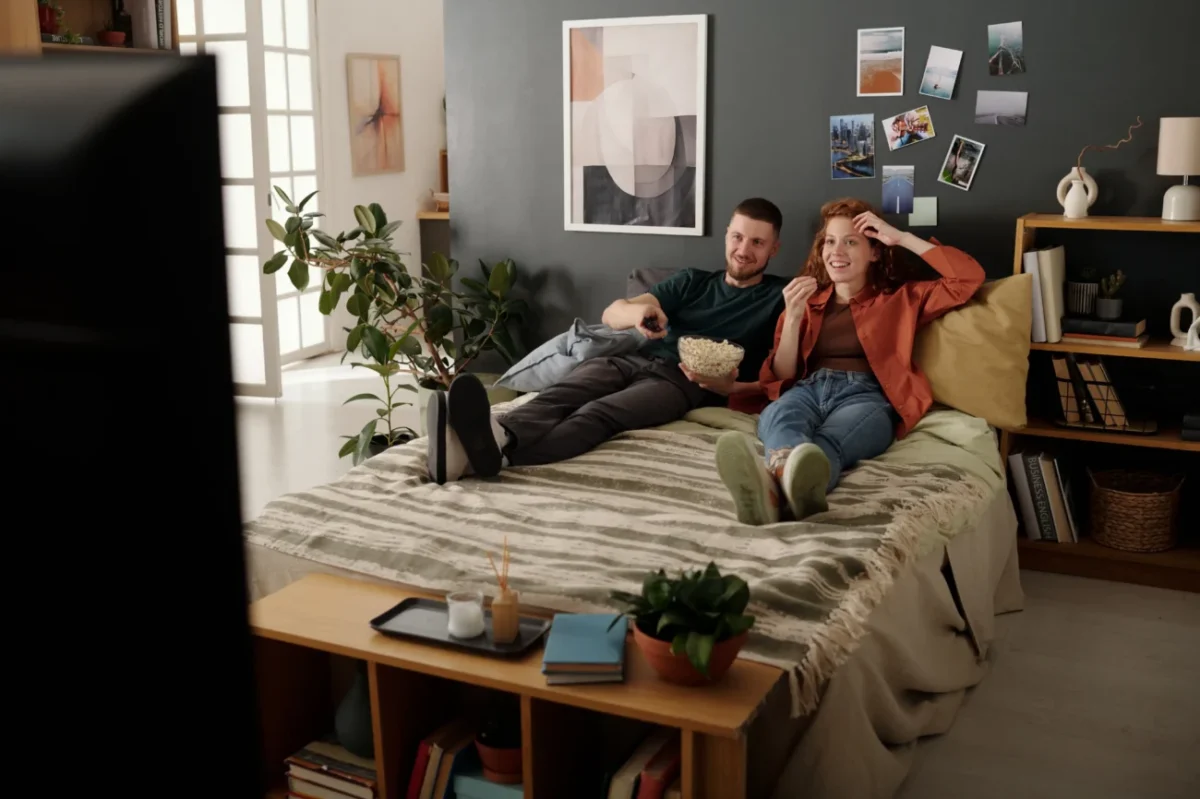 Žena a muž leží na posteli a dívají se na televizi.