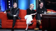 Tři herci sedící na červené sedačce.