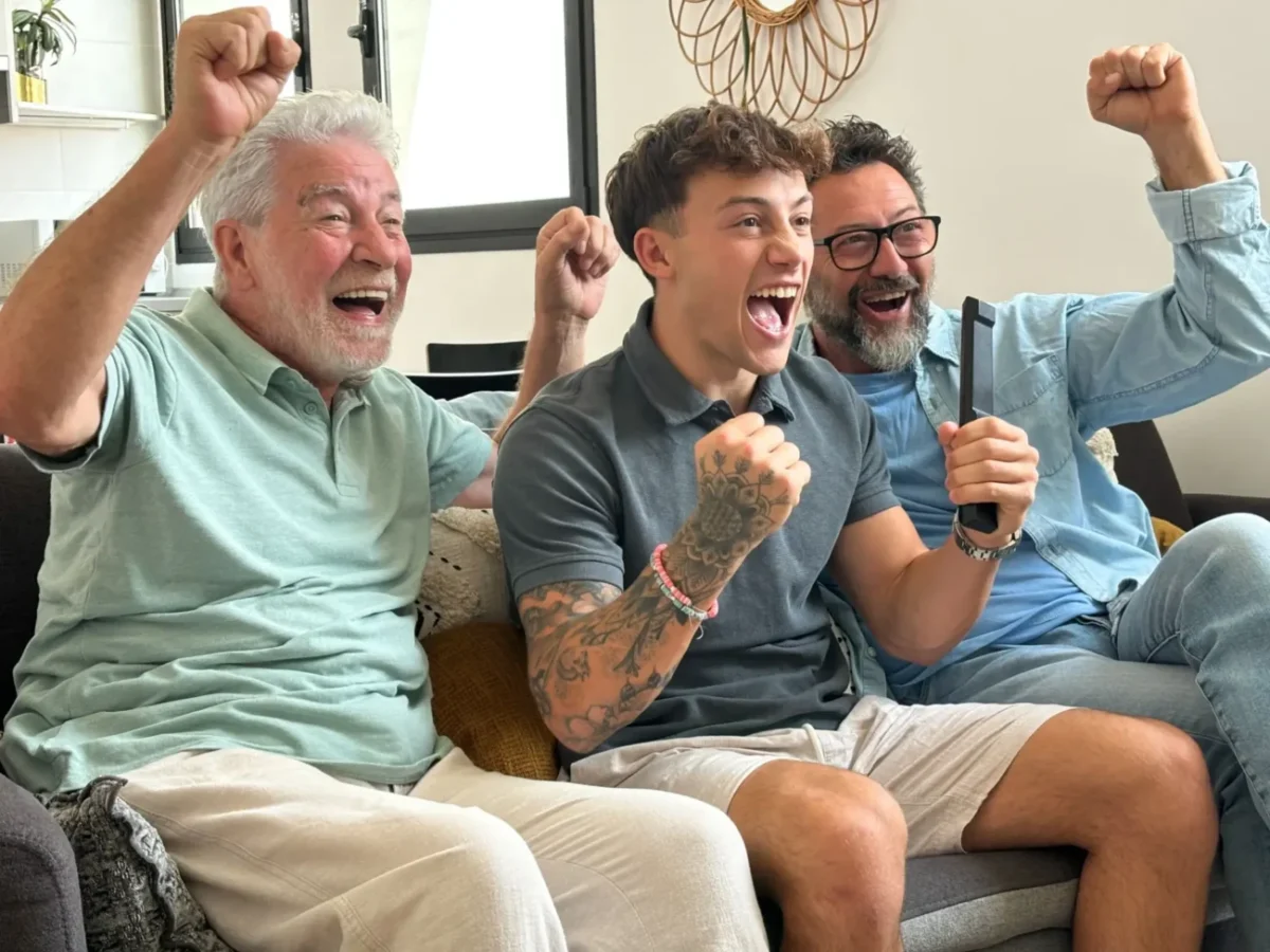 tři generace muží na gauči nadšeně sledují televizi