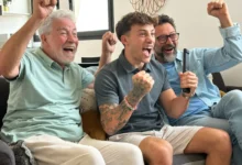 tři generace muží na gauči nadšeně sledují televizi