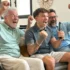 tři generace muží na gauči nadšeně sledují televizi