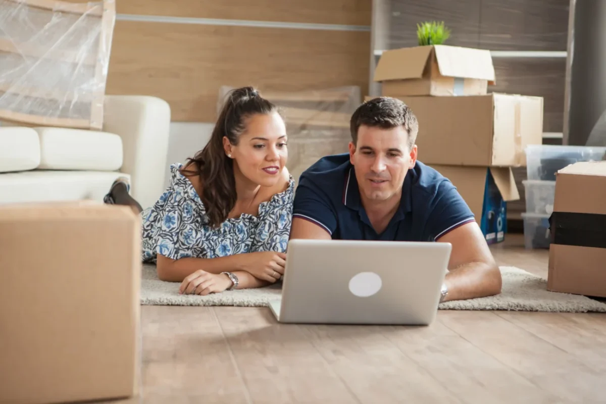 Muž a žena leží na zemi a koukají na notebook.