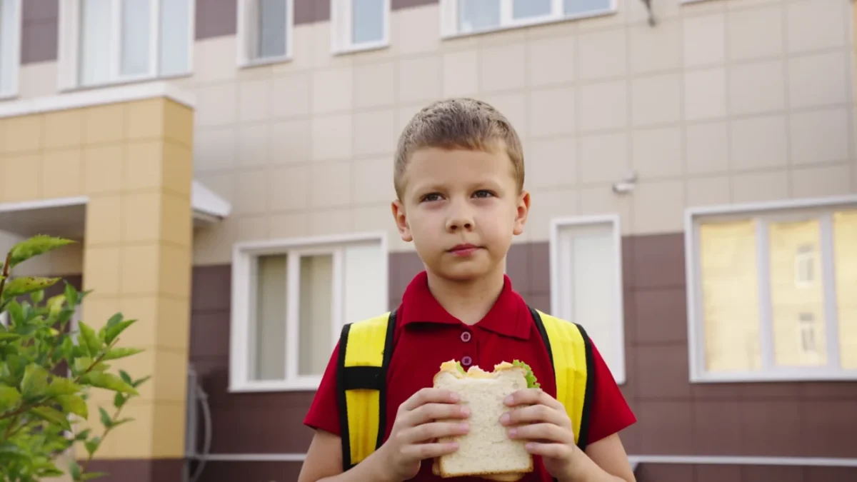Chlapec stojí před školou a jí toast.
