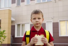 Chlapec stojí před školou a jí toast.