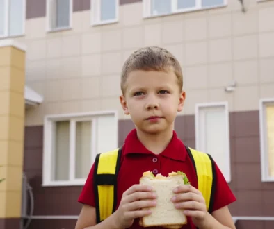 Chlapec stojí před školou a jí toast.