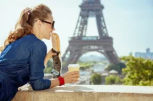 Žena si před Eiffelovkou dává kávu a bagetu.