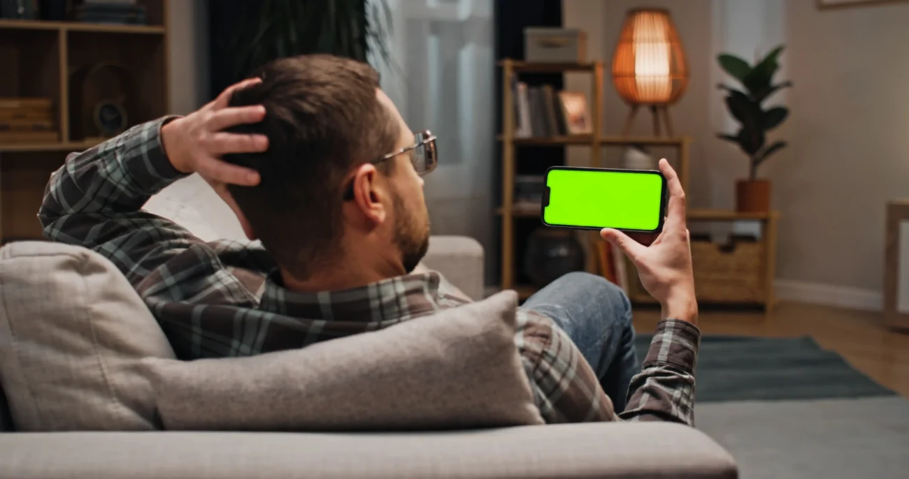 shutterstock_2558597393 | TVGURU.cz Muž se kouká na zelenou obrazovku telefonu.