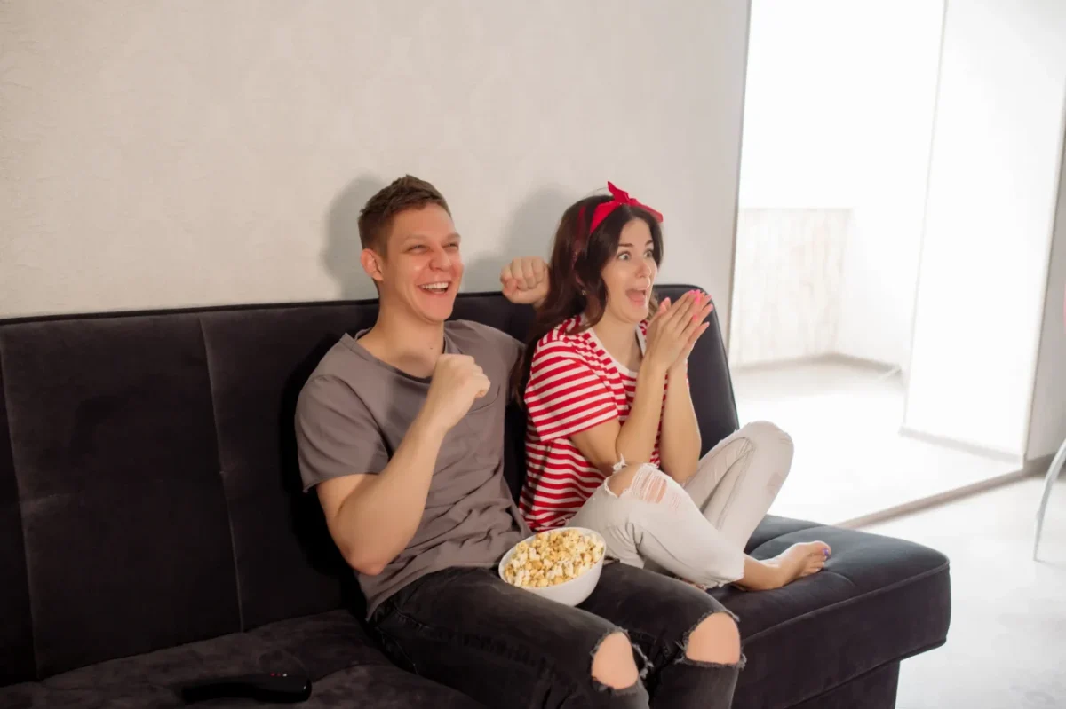 Mladí lidé sedí na gauči a smějí se něčemu v televizi.