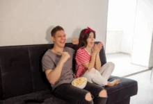 Mladí lidé sedí na gauči a smějí se něčemu v televizi.