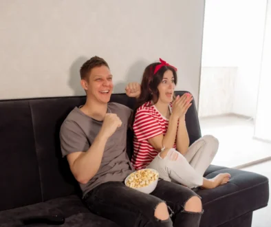 Mladí lidé sedí na gauči a smějí se něčemu v televizi.