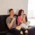 Mladí lidé sedí na gauči a smějí se něčemu v televizi.