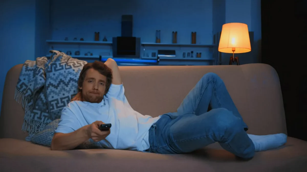 Nudící se muž dívající se na televizi.