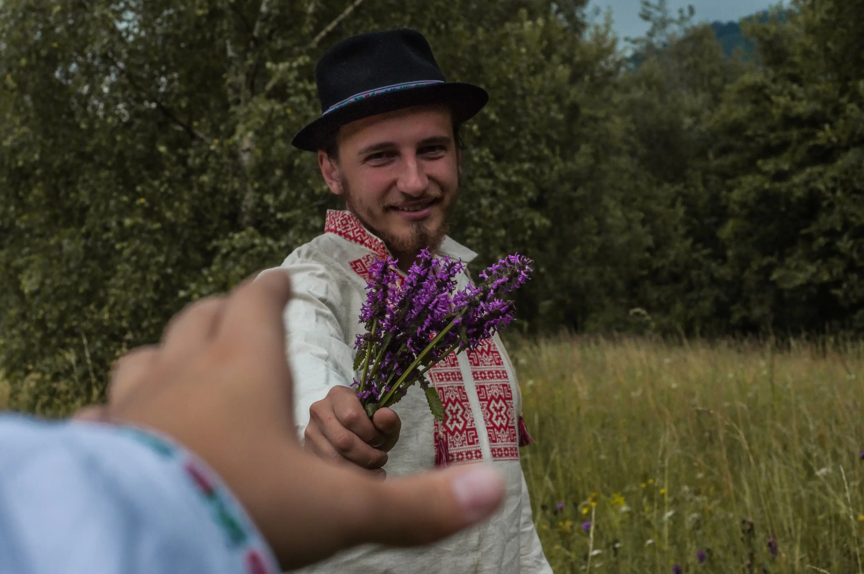 Muž ženě na louce podává kytičku. 