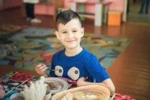 Chlapec sedí u stolu a jde jíst.