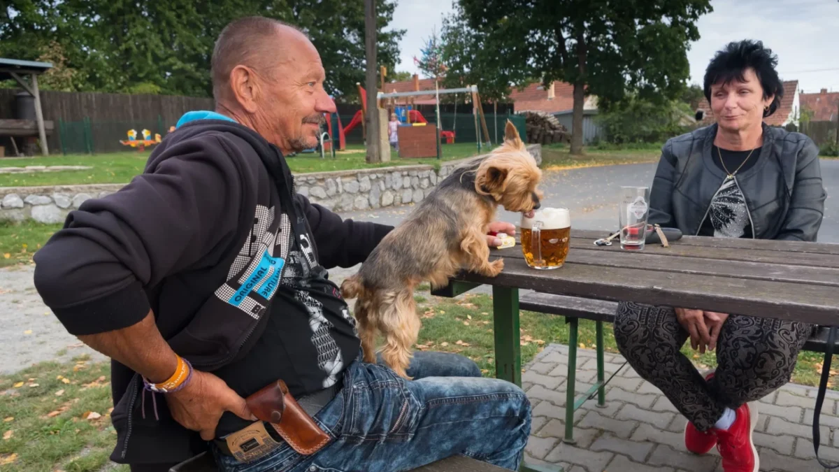 Češi s pejskem sedí venku na pivě.