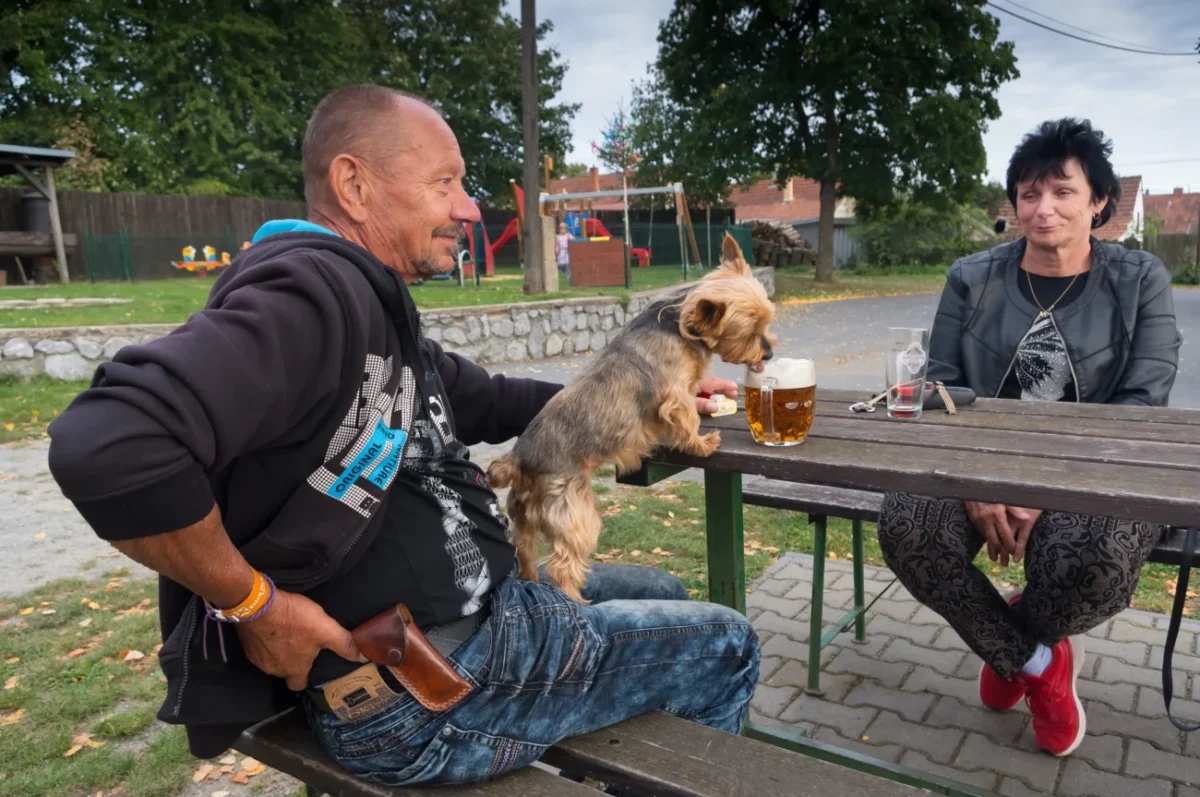 Češi s pejskem sedí venku na pivě.