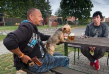 Češi s pejskem sedí venku na pivě.