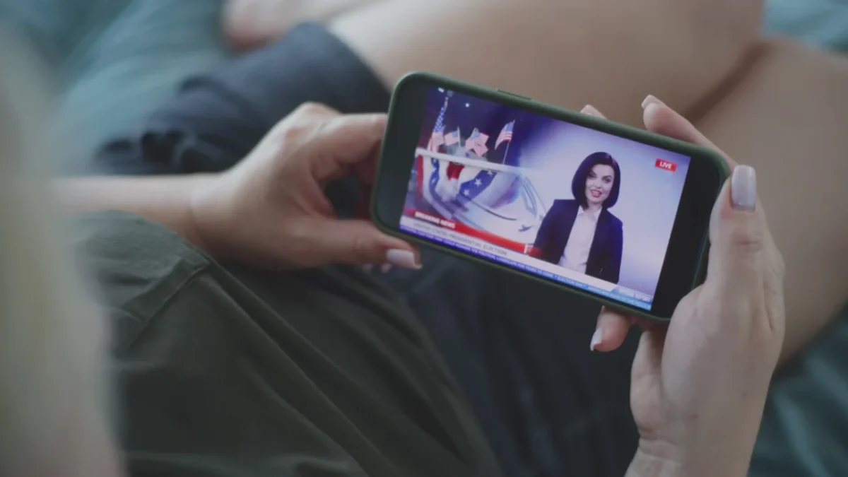 Ruce držící telefon s živým vysílláním.