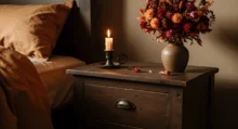 vintage tmavý noční stolek se zapálenou svíčkou a květinou ve váze s nečeksně tmavší zdí - v barvě kávy