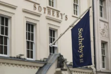 Bílé průčelí aukční síně Sotheby's s modrou vlajkou se zlatým nápisem.