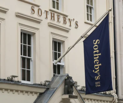 Bílé průčelí aukční síně Sotheby's s modrou vlajkou se zlatým nápisem.