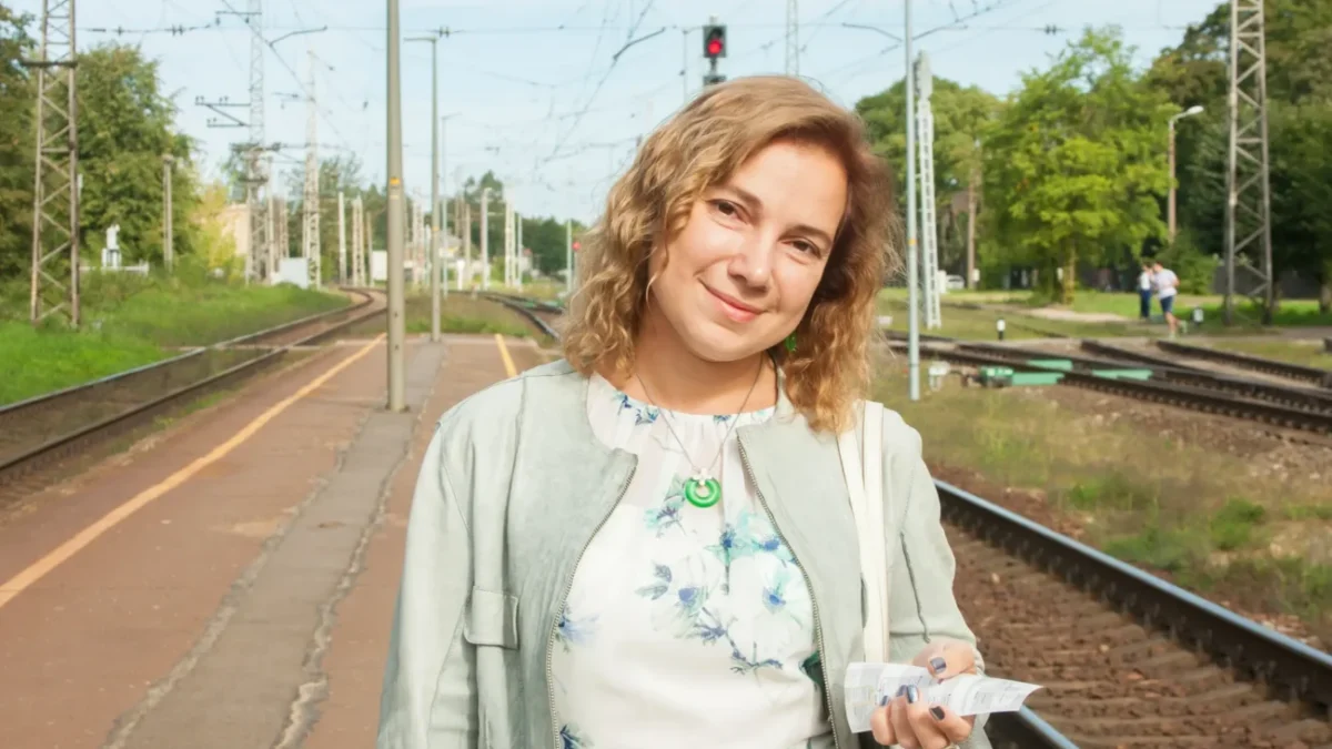 Žena stojí venku a dívá se přímo do kamery.