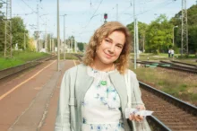 Žena stojí venku a dívá se přímo do kamery.