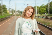 Žena stojí venku a dívá se přímo do kamery.