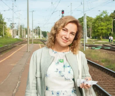 Žena stojí venku a dívá se přímo do kamery.