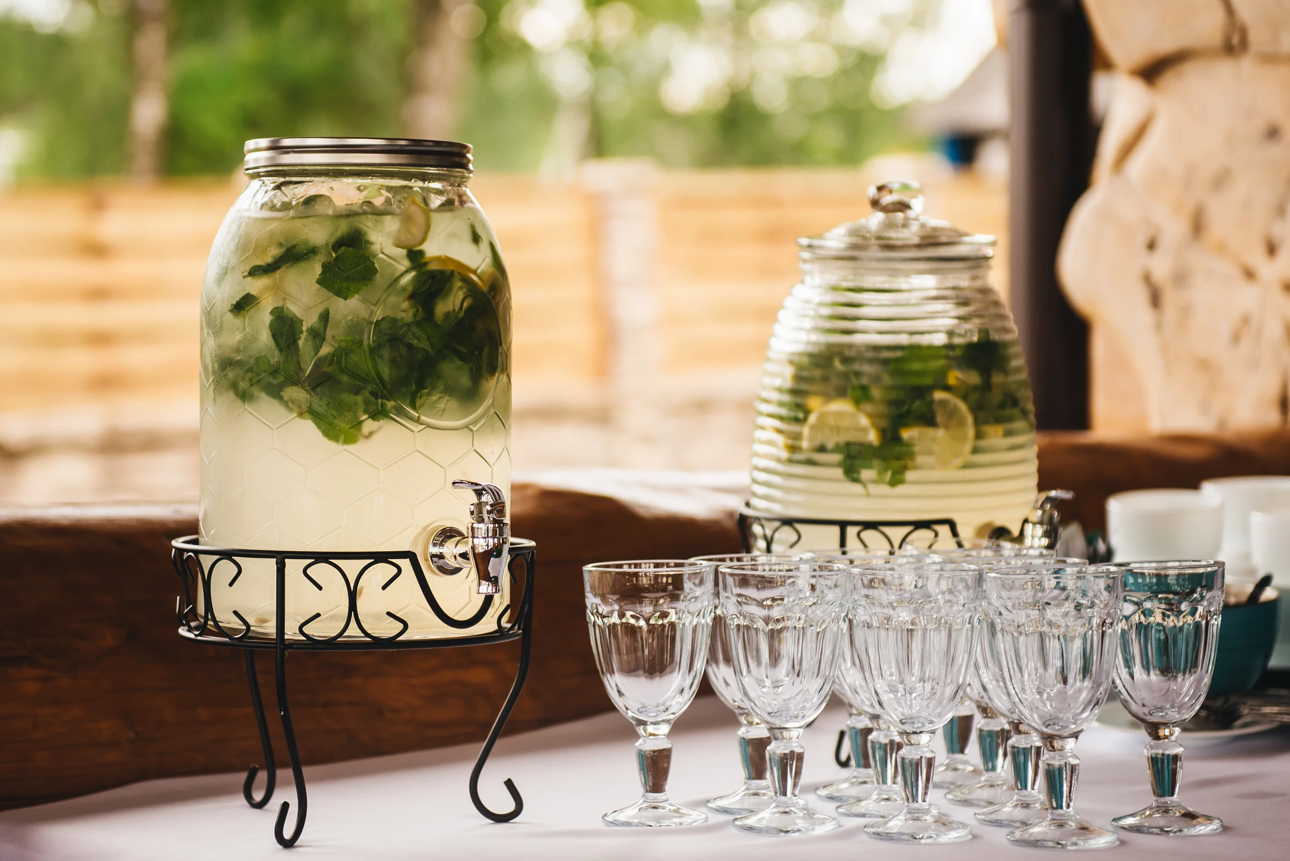 Domácí limonáda (okurka, citrusy) ve velké skleněné nádobě. Vedle toho broušené skleničky na stopce. Vše elegantní, luxusní