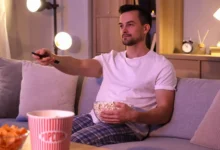 muž s popcornem z gauče sleduje televizi