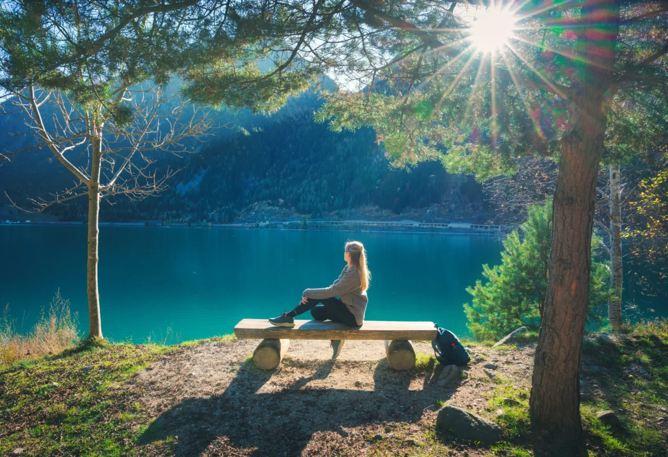 shutterstock_2599309225 1 1 | TVGURU.cz Žena sedí u jezera na lavičce.